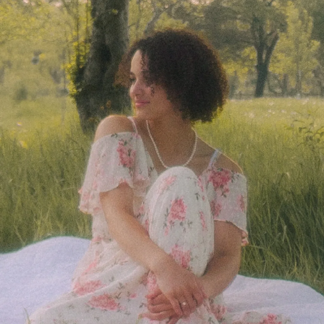 Elisha Antoine glancing over her shoulder, seated on a blanket in tall grass